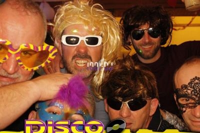 Des personnes déguisées avec des perruques, lunettes colorées et masques, posant dans une ambiance festive disco.