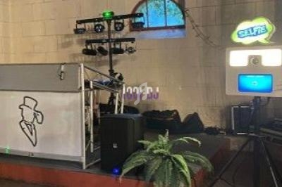 Cabine photo avec éclairage et borne selfie lumineuse, installée près d'une scène équipée de matériel de sonorisation.