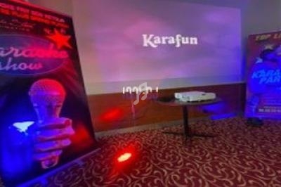 Écran de projection affichant ’Karafun’, entouré d'affiches promotionnelles de karaoké dans une salle éclairée.