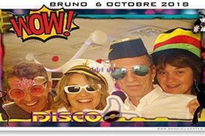 Quatre personnes déguisées avec des accessoires colorés posent devant un cadre photo à thème disco.