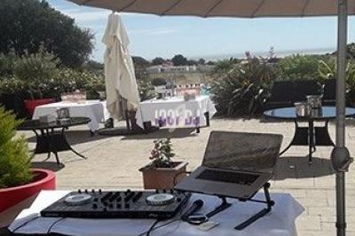 Poste de DJ avec platine et ordinateur portable sur une terrasse ensoleillée, entourée de tables et de plantes.