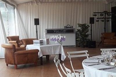 Salle aménagée avec des fauteuils en cuir, une table dressée, un espace DJ et des éclairages pour un événement.