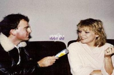 Un homme interviewe une femme assise, micro en main, dans un cadre intérieur sobre.