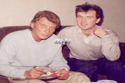 Deux hommes assis sur un canapé, l'un signant un objet et l'autre posant à ses côtés.