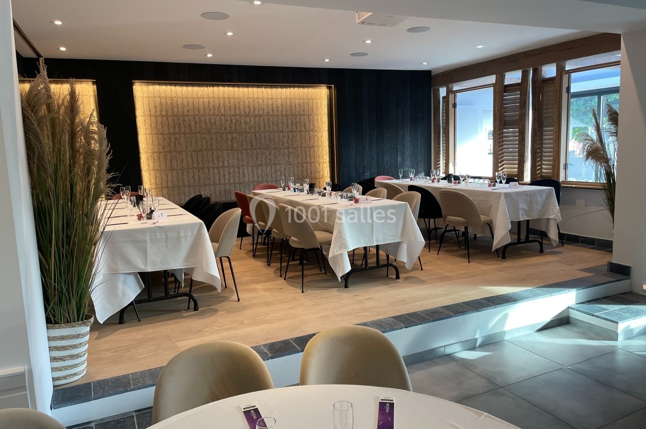 Salle de restaurant élégante avec tables dressées, nappes blanches, éclairage chaleureux et grandes fenêtres.
