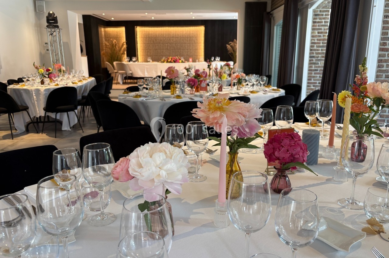 Tables élégamment dressées avec des fleurs colorées dans une salle lumineuse, préparée pour un événement festif.