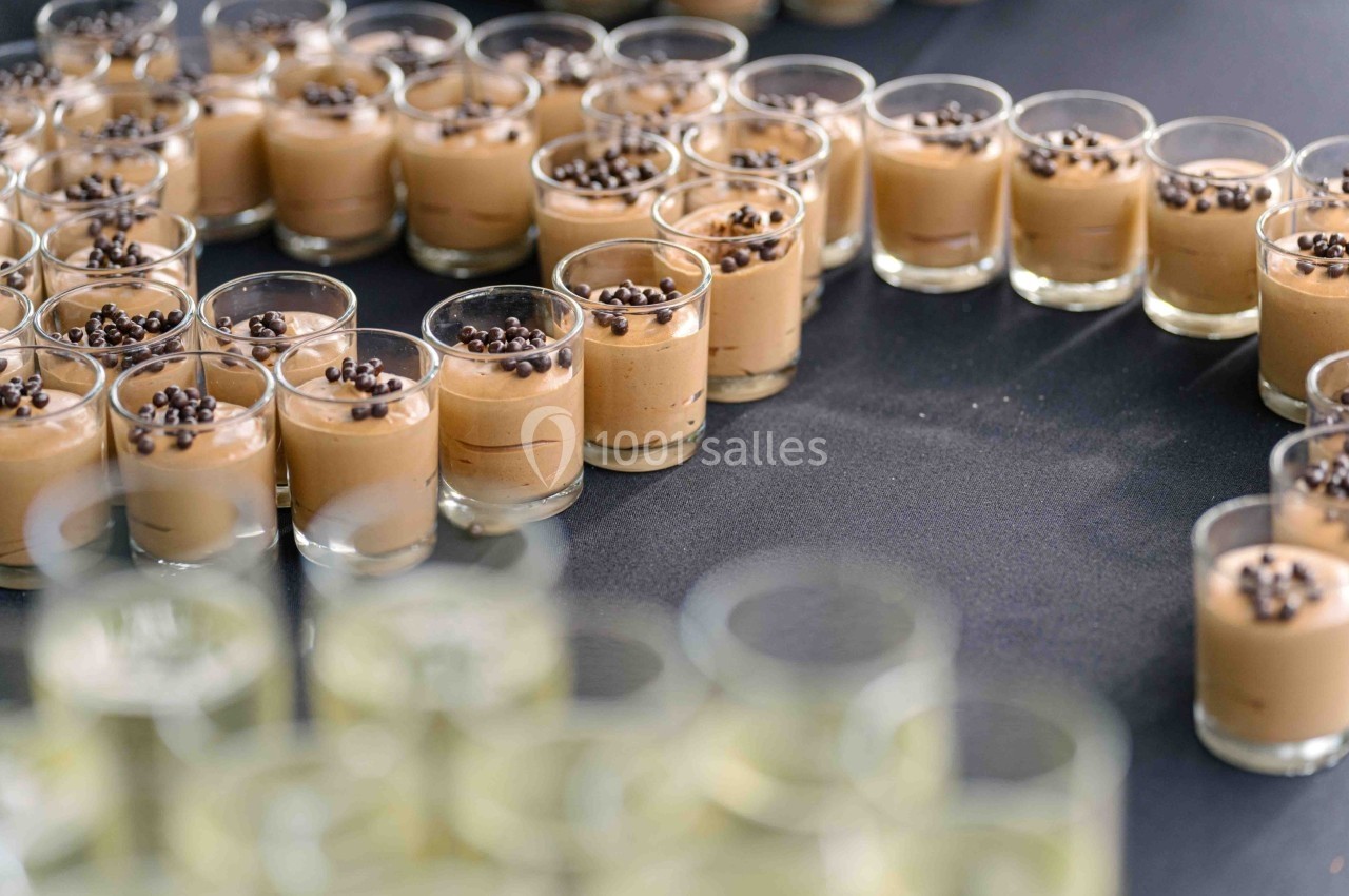 Petits verres de mousse au chocolat garnis de pépites de chocolat, disposés en cercle sur une table noire.
