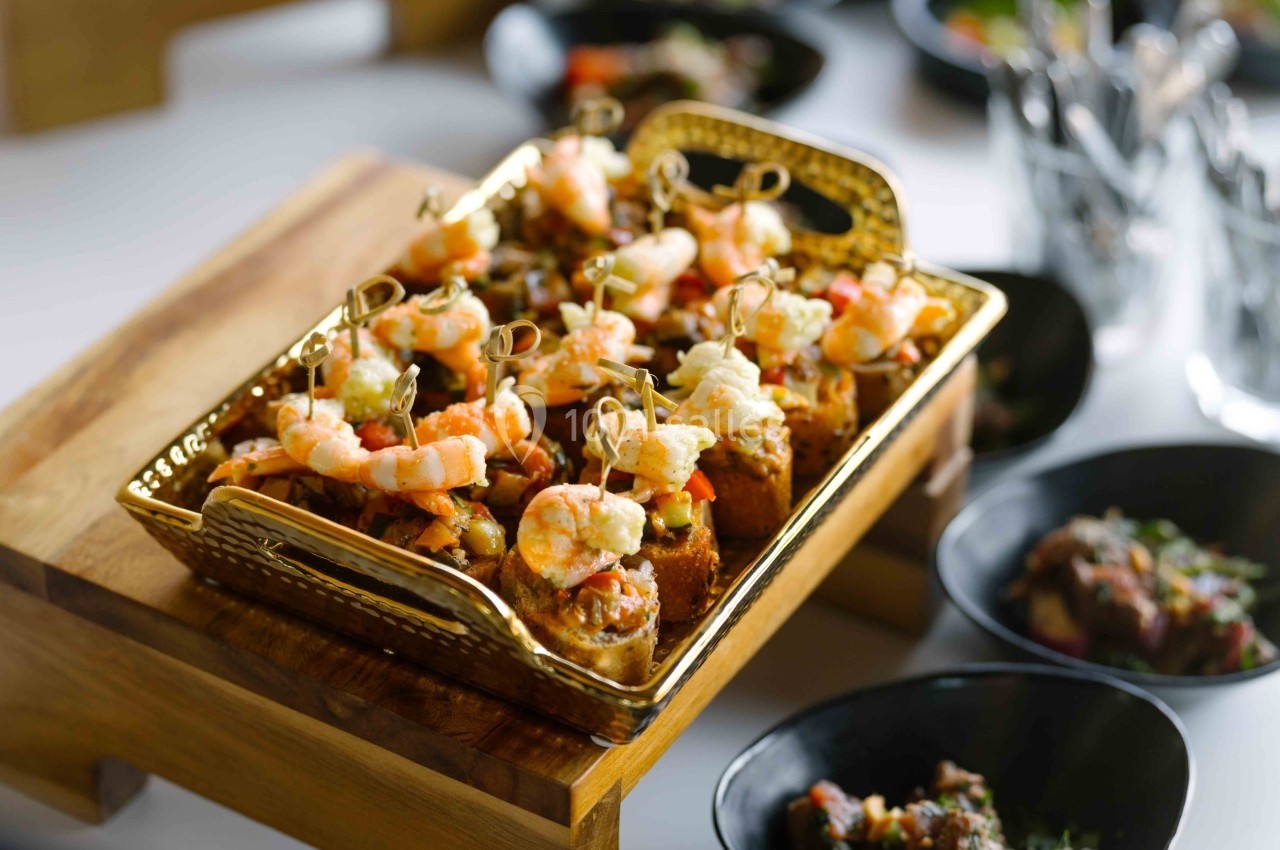 Plateau doré contenant des bouchées apéritives garnies de crevettes et de légumes, présenté sur une table.