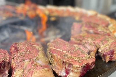 Viande rouge assaisonnée en train de griller sur une plaque chauffante au-dessus d'un feu de bois.