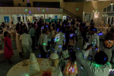 Des invités dansent et discutent dans une salle de réception décorée, éclairée par des lumières colorées.