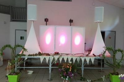 Installation de matériel de sonorisation et éclairage sur une scène décorée avec des guirlandes et des plantes.