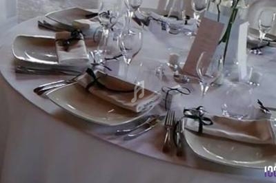 Table ronde dressée avec nappes blanches, assiettes, couverts, verres et serviettes nouées de rubans noirs.