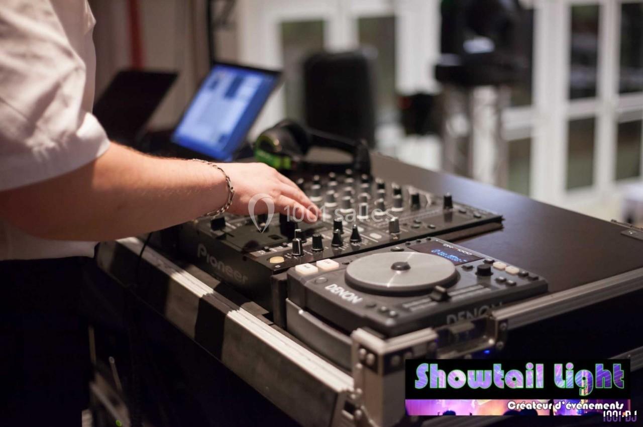 Un DJ manipule une table de mixage avec des équipements audio dans un environnement intérieur.