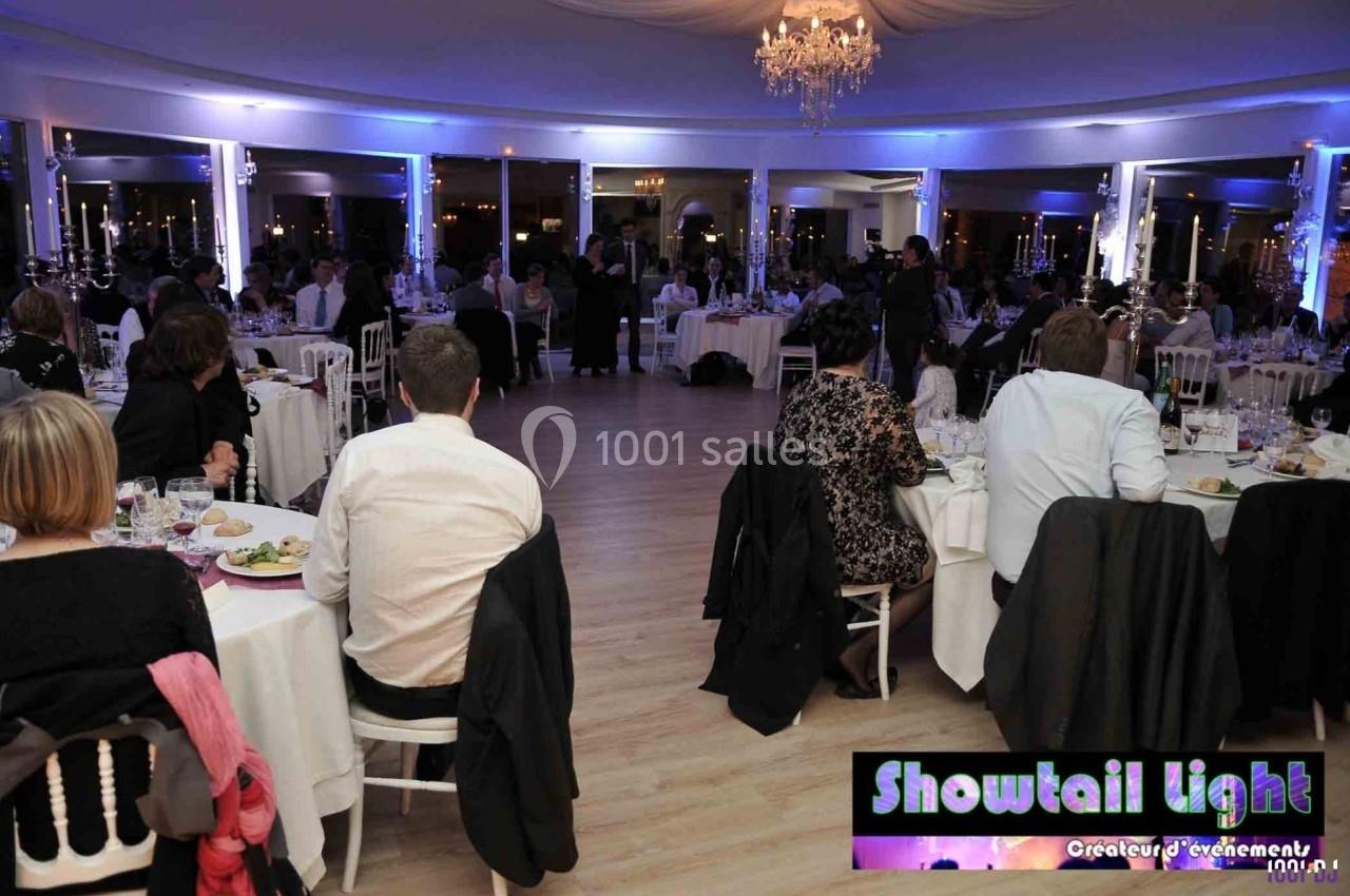 Salle de réception éclairée en bleu, avec des invités assis à des tables rondes lors d'un dîner ou événement.