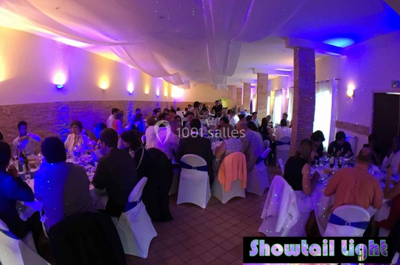 Salle de réception avec des invités assis à des tables rondes, éclairage tamisé et ambiance festive.