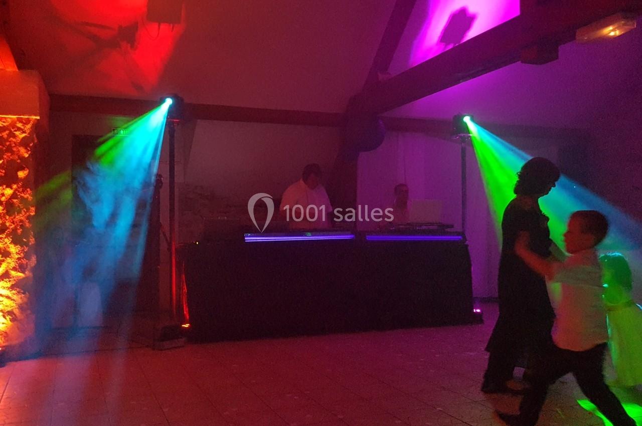 Personnes dansant devant un DJ avec des jeux de lumière colorés dans une salle sombre.
