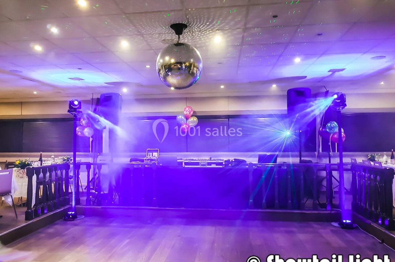 Salle de fête avec piste de danse, éclairage violet, boule disco suspendue et équipement de DJ en arrière-plan.