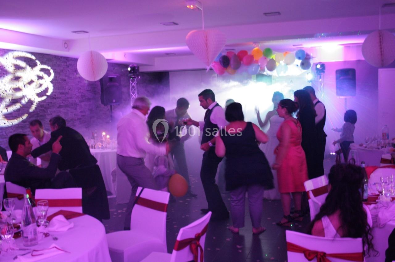 Des personnes dansent dans une salle décorée avec des lumières colorées, des ballons et des guirlandes suspendues.