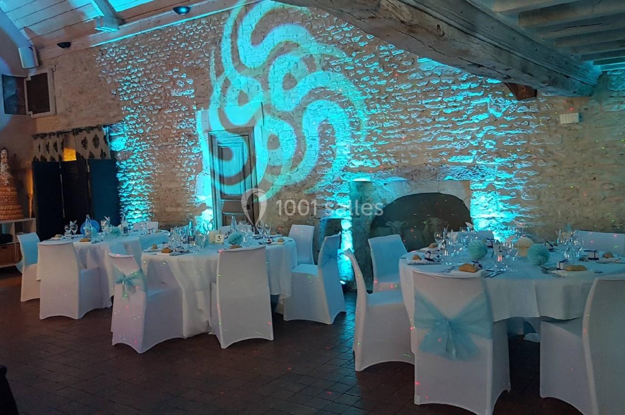 Salle de réception décorée avec des tables dressées, éclairage bleu et motifs lumineux projetés sur les murs en pierre.