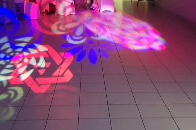 Des personnes dansent dans une salle sombre éclairée par des faisceaux lumineux colorés et des effets laser.