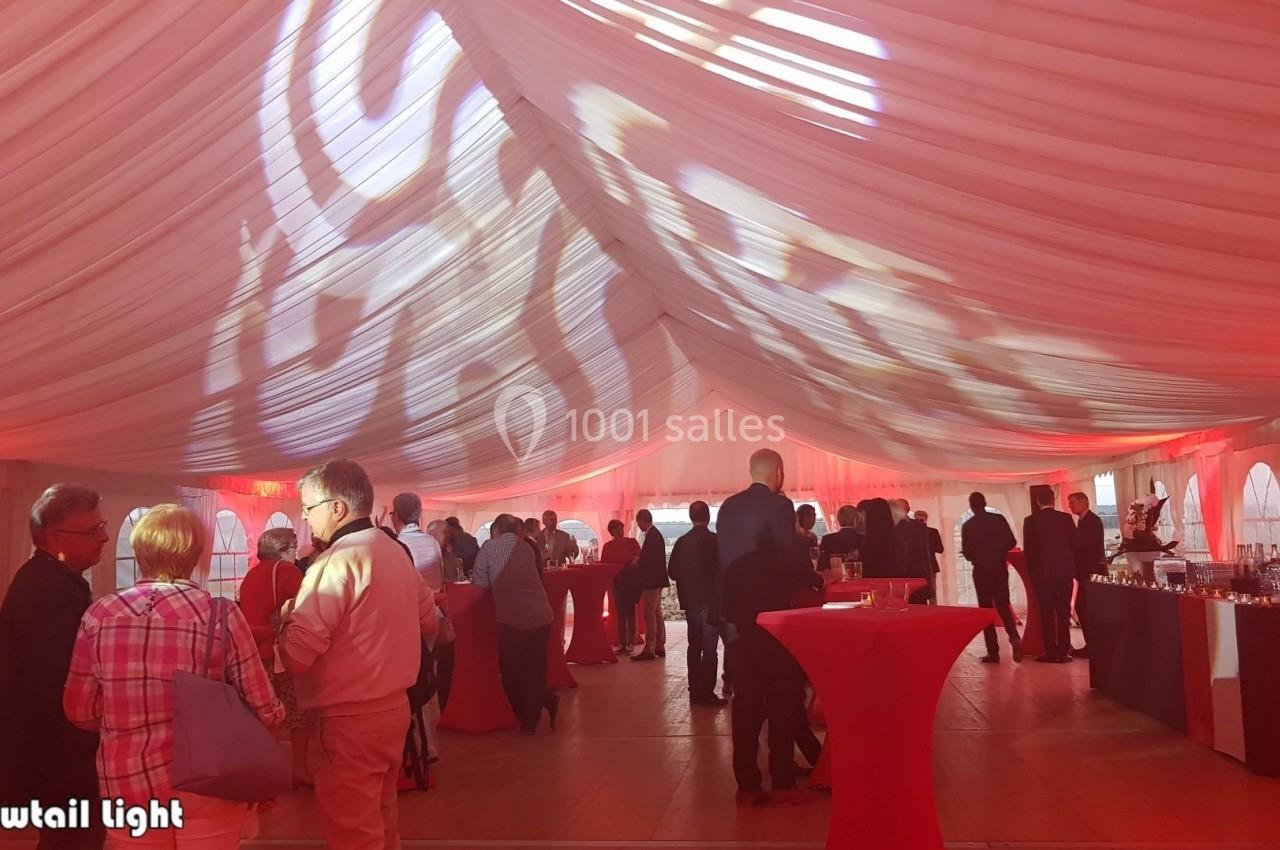 Personnes réunies dans une tente éclairée par des lumières rouges et blanches, avec des tables hautes et un buffet.
