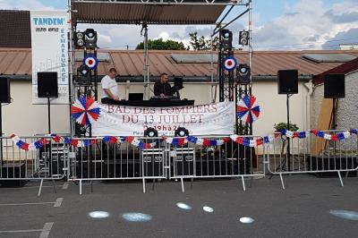 Cube lumineux coloré disposé sur une terrasse en soirée, près d'une tente blanche et d'une table dressée.