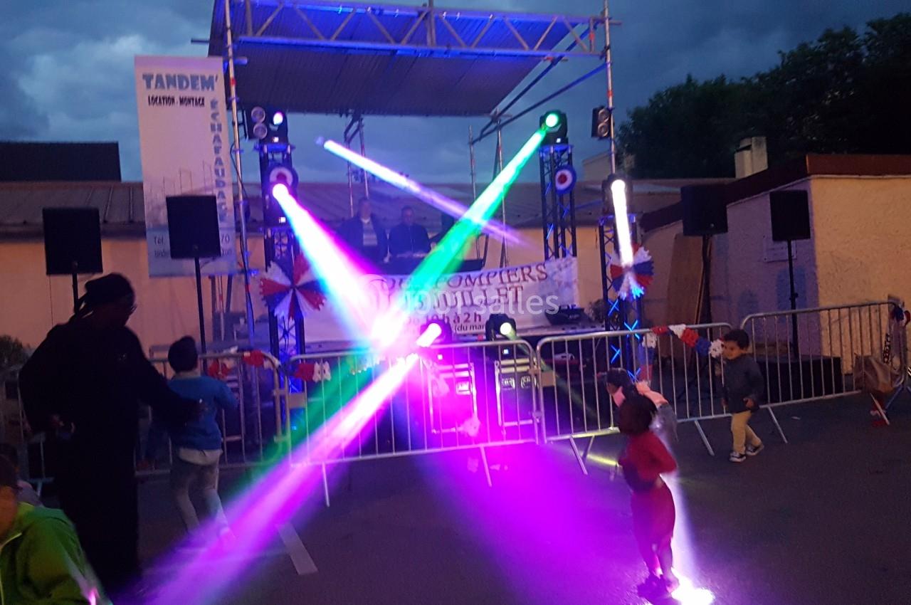 Scène extérieure avec jeux de lumière colorés, enfants jouant au premier plan et ciel nuageux en arrière-plan.