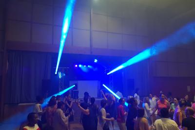 Cube lumineux coloré disposé sur une terrasse en soirée, près d'une tente blanche et d'une table dressée.