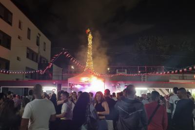 Cube lumineux coloré disposé sur une terrasse en soirée, près d'une tente blanche et d'une table dressée.