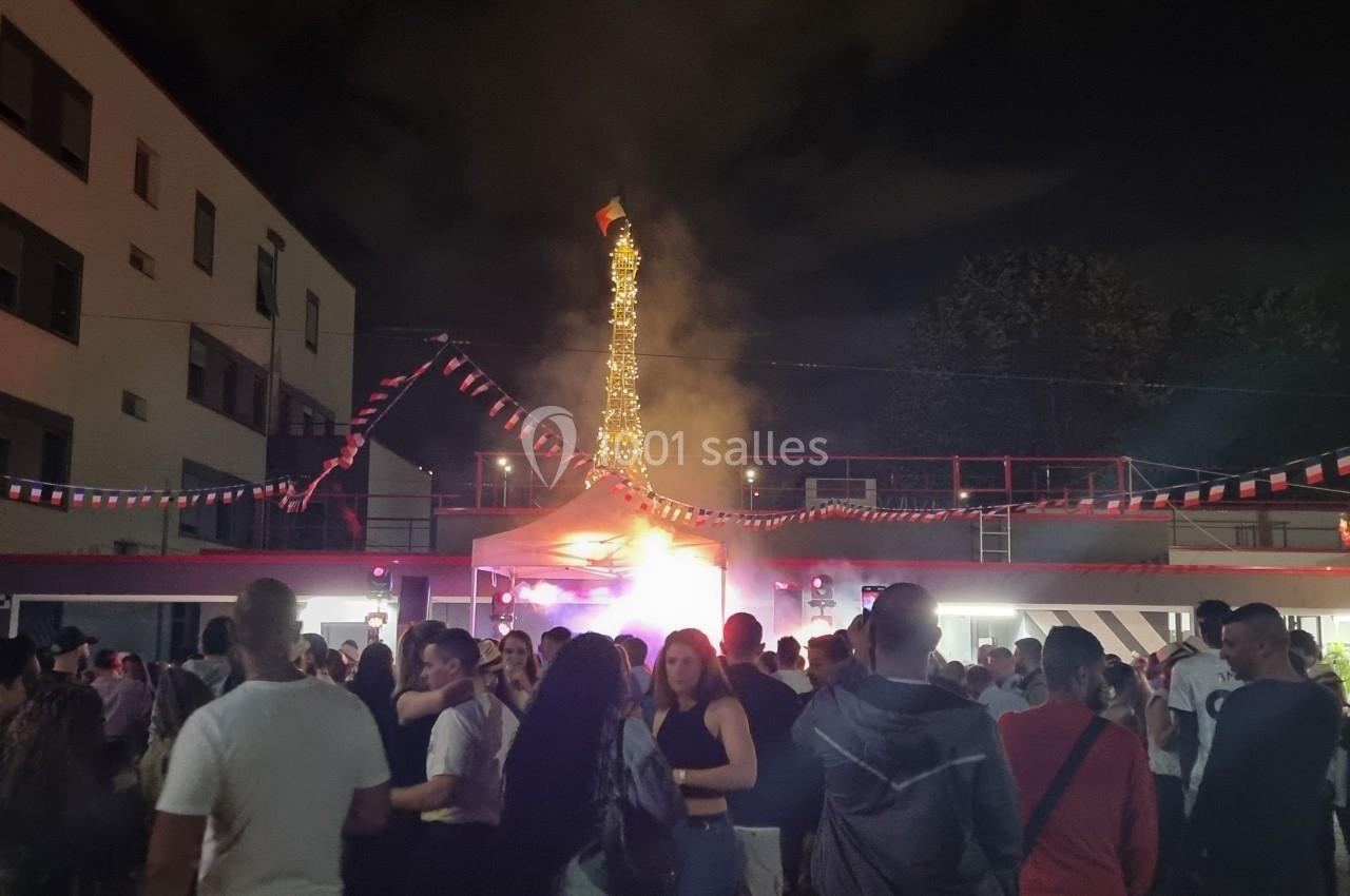 Foule rassemblée de nuit dans une cour décorée de guirlandes, avec une structure illuminée en arrière-plan.