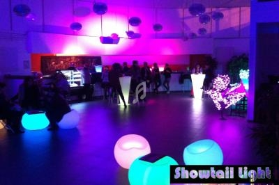 Salle tamisée avec éclairage coloré, mobilier lumineux et groupes de personnes discutant autour de tables hautes.