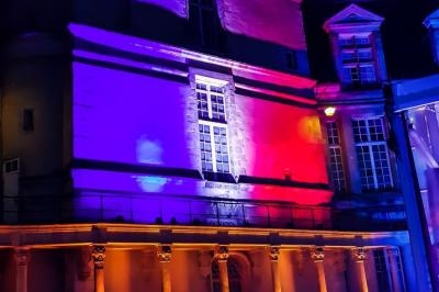 Façade d'un bâtiment historique éclairée par des lumières colorées rouge, bleu et violet durant la nuit.