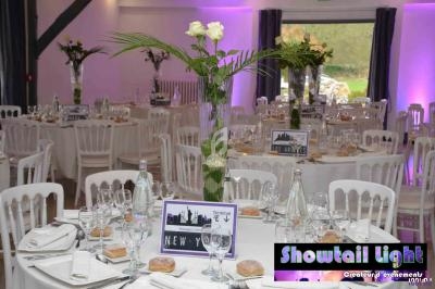 Salle de réception décorée avec des tables rondes, nappes blanches, centres de table fleuris et ambiance lumineuse.