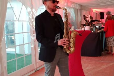 Un musicien jouant du saxophone dans une tente événementielle, près d'une table haute rouge.