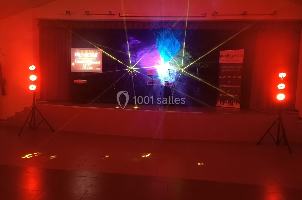 Scène éclairée par des projecteurs rouges et des faisceaux lumineux, avec écrans et rideaux en arrière-plan.