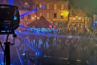 Salle de réception décorée avec des tables rondes, nappes blanches, chaises transparentes et éclairage rose.