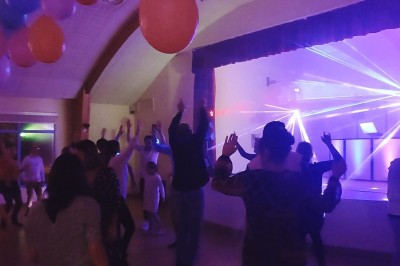 Salle de réception décorée avec des tables rondes, nappes blanches, chaises transparentes et éclairage rose.