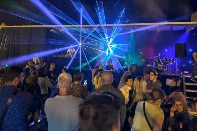 Salle de réception décorée avec des tables rondes, nappes blanches, chaises transparentes et éclairage rose.