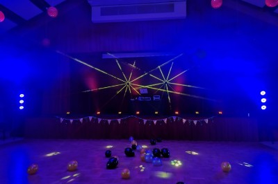 Salle de réception décorée avec des tables rondes, nappes blanches, chaises transparentes et éclairage rose.