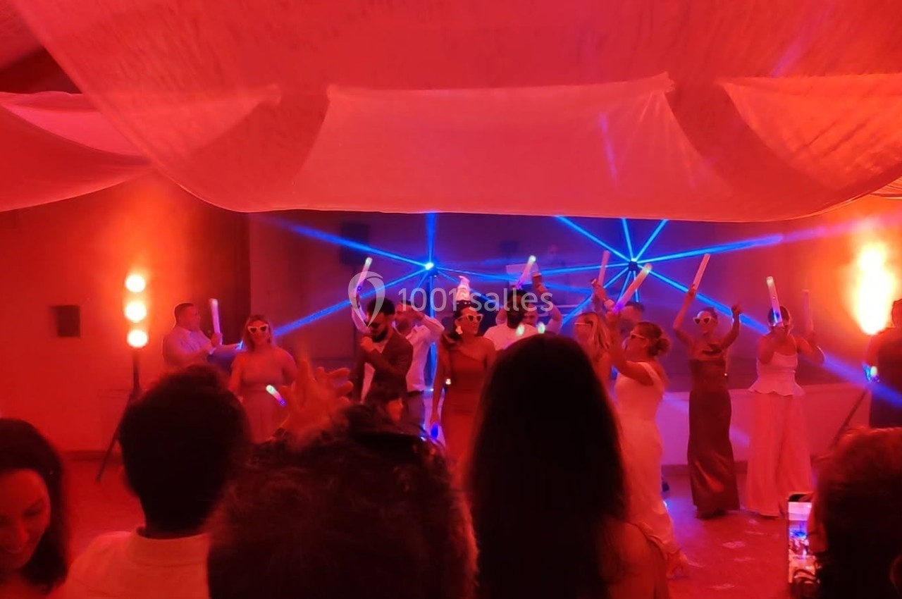 Groupe de personnes dansant sous des lumières colorées et des faisceaux laser dans une salle décorée de voilages.