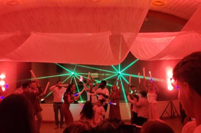 Salle de réception décorée avec des tables rondes, nappes blanches, chaises transparentes et éclairage rose.