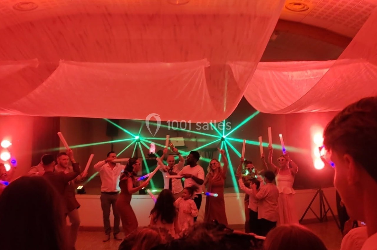 Des personnes dansent sous des lumières colorées et des lasers lors d'une fête ou d'un événement festif en intérieur.