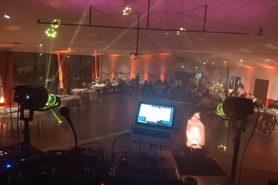 Salle de réception décorée avec des tables rondes, nappes blanches, chaises transparentes et éclairage rose.