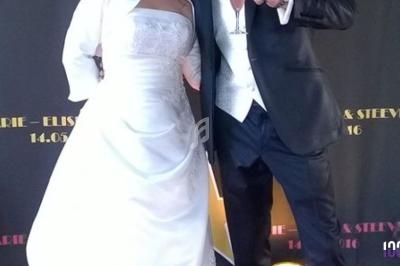 Un couple en tenue de mariage pose devant un panneau décoratif indiquant leurs prénoms et la date de l'événement.