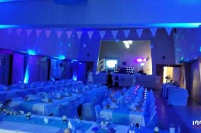 Salle de réception décorée en bleu avec tables dressées et guirlandes lumineuses suspendues.