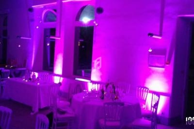 Salle de réception décorée avec des lumières violettes, tables dressées avec chaises blanches et grandes fenêtres en arrière…