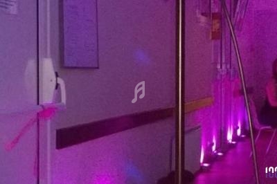 Couloir éclairé par des lumières violettes, avec une femme assise sur une chaise à droite.