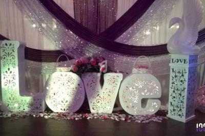 Décoration de mariage avec des lettres lumineuses formant ’LOVE’, des cygnes blancs et des pétales de fleurs au sol.