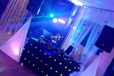 Installation de DJ avec table lumineuse, enceintes et décorations festives dans une salle éclairée par des jeux de lumière.