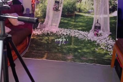 Fond de studio représentant une arche décorée de fleurs et de lanternes sur une pelouse, avec un trépied au premier plan.